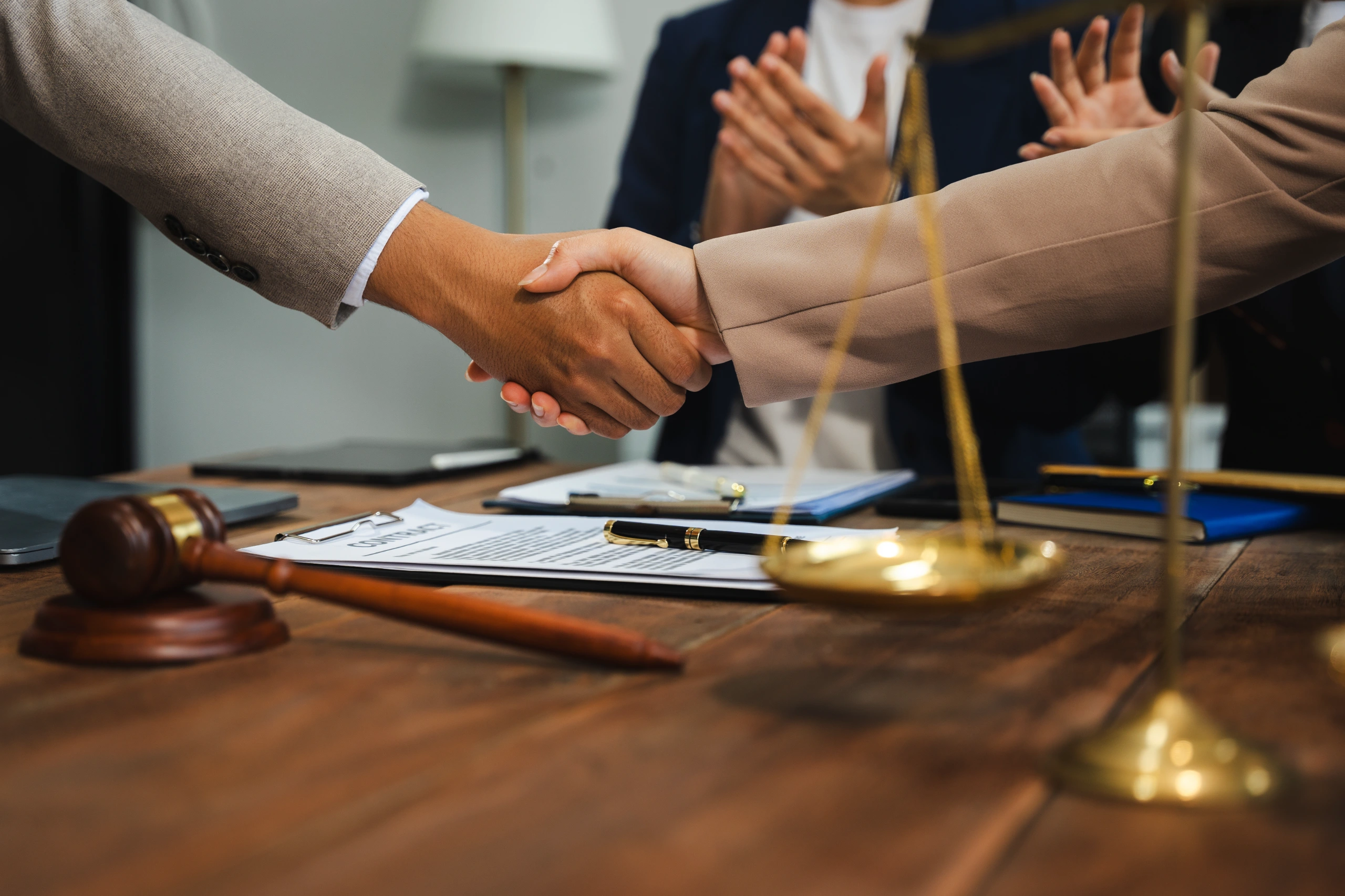 Close-up of handshake over legal documents with gavel and scales.